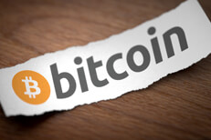 Bitcoin logo on torn scrap of paper Bitcoin cryptocurrency logo printed on torn piece of scrap paper lying on woodgrain surface