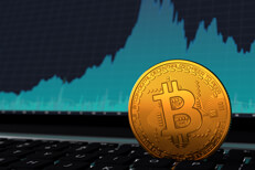 Bitcoin vertical on laptop keyboard in front of blue price volatility area chart on screen