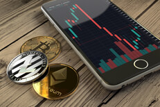 Bitcoin, Ethereum, and Litecoin coins next to iPhone showing candlestick stock chart