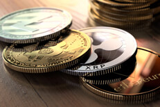 Bitcoin, Ripple, Litecoin, and Ethereum coins in front of stack of Bitcoins