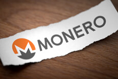 Monero altcoin cryptocurrency logo printed on torn piece of scrap paper on woodgrain surface
