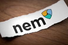 Nem altcoin cryptocurrency logo printed on torn piece of scrap paper on woodgrain surface