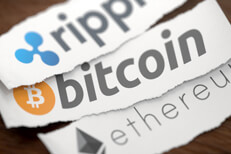 Ripple, Bitcoin, and Ethereum cryptocurrency logos printed on torn pieces of white scrap paper on woodgrain surface