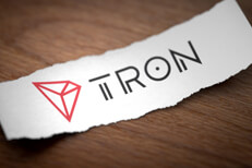 Tron altcoin cryptocurrency logo printed on torn piece of scrap paper on woodgrain surface