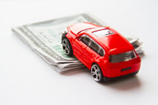 Toy car climbing folded money Red toy car climbing folded 100 dollar bills automotive cost concept