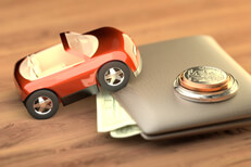 Toy car climbing wallet with coins Toy car climbing wallet with small stack of coins on top symbolizing the cost of auto insurance