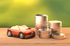 Red toy car next to stacks of coins Small red toy car next to stacks of coins on wood table with nature background