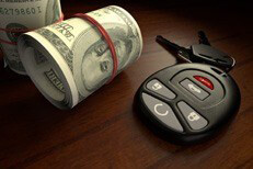 High cost of car insurance Cost of insurance concept showing two rolls of money next to car keys on desk