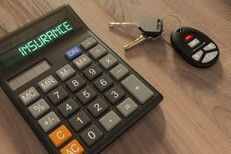 Insurance calculator and car keys on wood desk in morning light