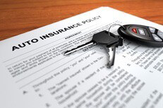 Auto insurance policy on desk with car keys and door clicker