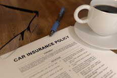 Car insurance policy on desk with coffee, glasses, and pen