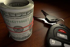 Roll of one hundred dollar bills wrapped in rubber bank with car keys on wood table