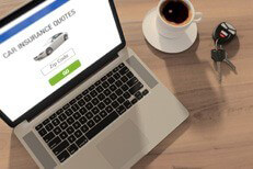 Laptop with car insurance quote website, cup of coffee, and car keys on wood table