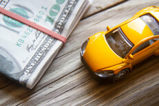 Toy car next to folded currency bills Yellow toy car next to folded 100 dollar bills car insurance or automotive costs concept photo