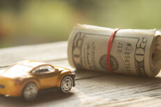 Small car next to roll of money Small toy car next to roll of money wrapped in rubber bands