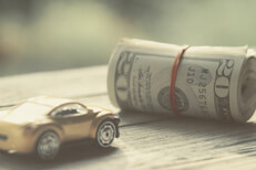 Vintage photo of small toy car next to roll of money wrapped in rubber bands