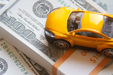 Yellow toy car on top of $10,000 cash bundle car insurance or automotive cost concept photo