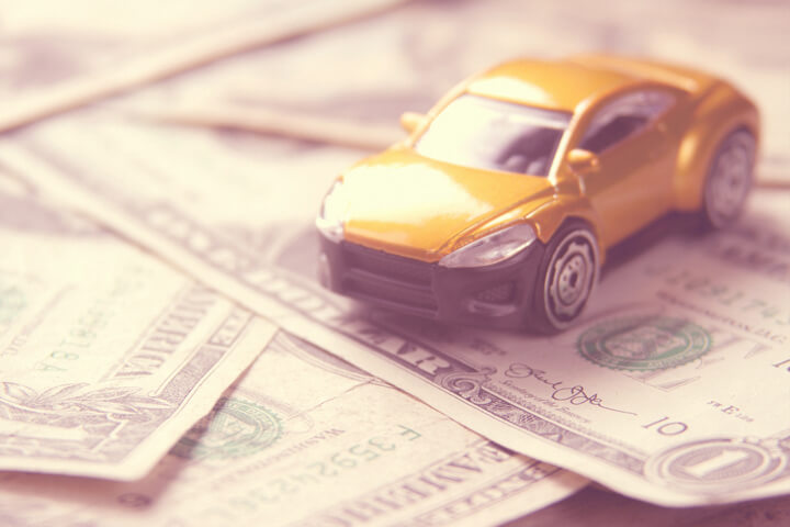 Small car on scattered dollar bills illustrating automotive cost or auto insurance cost