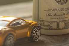 Small yellow car next to upright money roll on wood background
