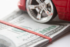 Close view of chrome car wheel and tire resting on folded 100 dollar bills with rubber band
