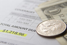 Car insurance bill showing total amount due with dollar bills and a quarter