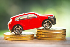 Red toy car on two stacks of gold coins Red toy car on two increasing stacks of gold coins with blurred nature background