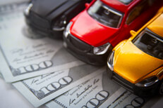 Photo of black, yellow, and red toy cars on fanned out 100 dollar bills