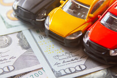 Three toy cars on 100 dollar bills Photo of black, yellow, and red toy cars on scattered 100 dollar bills