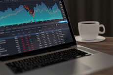 Laptop with stock research Laptop on table with coffee mug showing stock price information and area chart