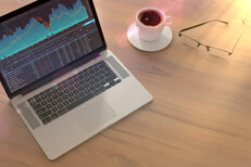 Investment laptop on table with flare Laptop with stock price screen on table with glasses and coffee cup with lighting flare effect