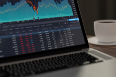 Laptop with stock prices and coffee Laptop showing stock prices and area chart with coffee cup in background