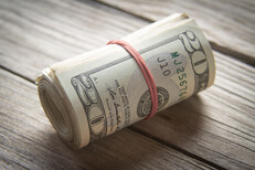 Roll of twenty dollar bills Roll of 20 dollar bills with rubber band on wood background