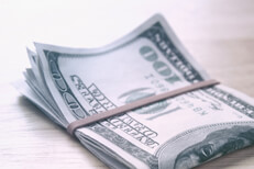 $100 bills folded on wood table $100 bills folded with rubber band on wood table