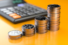Quarters stacked in front of calculator Four increasing stacks of U.S. quarters in front of calculator on orange reflective background