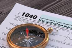 Navigational compass lying on IRS form 1040 on word wood plank background