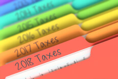 Photo of prior tax year rainbow-colored manila folder tabs in filing cabinet