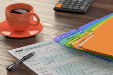 Desk with tax folders, 1040 form, calculator, and coffee lit by background window light