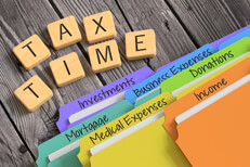 Stack of tax folders on worn wood planks next to wooden letters spelling tax time