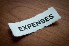 Torn piece of paper with word Expenses with depth of field blur and woodgrain background