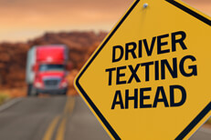 Yellow road sign reading Driver Texting Ahead with oncoming semi truck in blurred in background